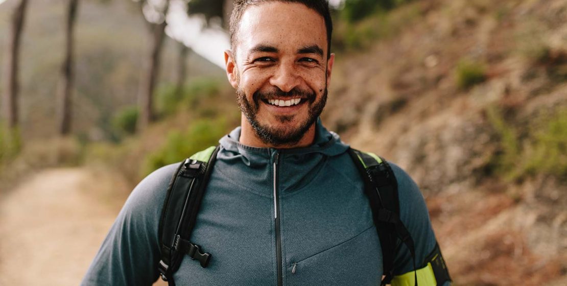 Portrait of young man standing outdoors and smiling. Confident male runner on country road.