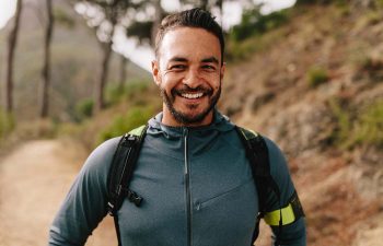 Portrait of young man standing outdoors and smiling. Confident male runner on country road.