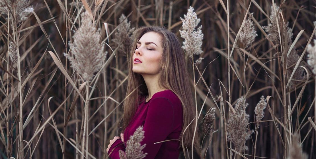 Girl with long hair wearing red shirt in forest field among large tall plants grass.