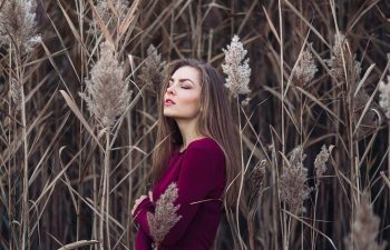 Girl with long hair wearing red shirt in forest field among large tall plants grass.