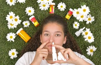 A woman using a nasal spray and surrounded by bottles of medicines.