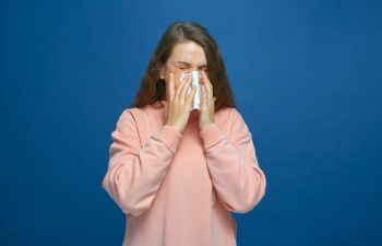 Girls with stuffy nose blowing nose into tissue.