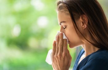 Woman suffering from allergy blowing her nose while walking in a park.
