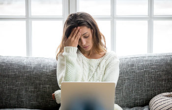 concerned woman touches her head sitting with laptop on the couch